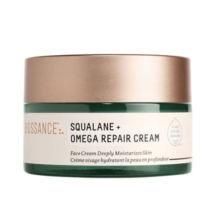 A tub of Biossance Squalane + Omega Repair Cream. The round tub is green with a cream label and gold lid.