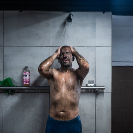 a coal miner takes a shower in a communal shower after his shift. He is covered in black coal dust.