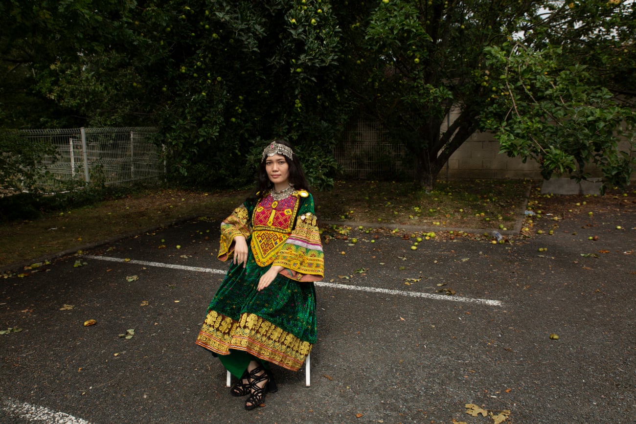 Shegofa Ibrahimi, an actor and musician, sits on a chair in a car park wearing traditional dress.