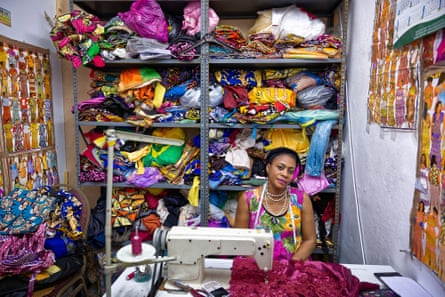 Woman sits behind a sewing machine surrounded by shelves of brightly coloured fabric