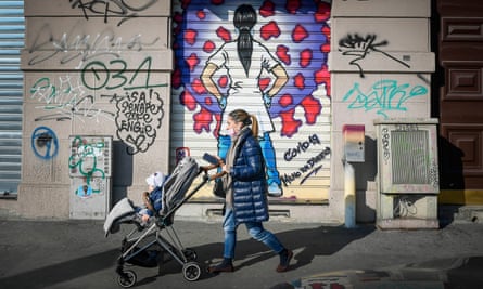 A woman and her child pass Covid-19 street artwork on the shutter of a shop in Milan.