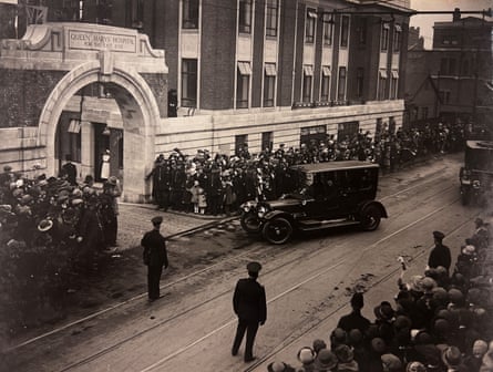 A sepia-tinted photograph of a car turning to pass through the arch, as crowds of people line the street