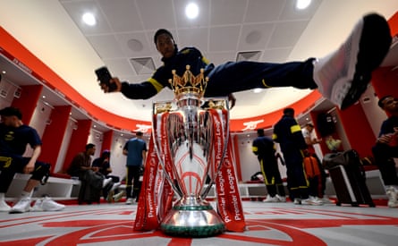 Myles Lewis-Skelly jumps over the Premier League trophy in the Arsenal dressing room before the parade