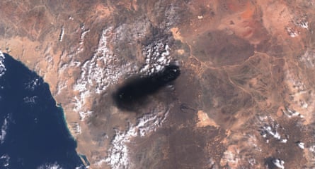 Satellite image of black smoke over brown ground with sea to the west