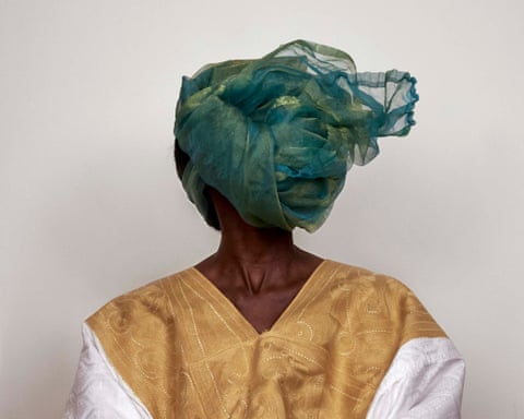 A person's face is covered by a draped green sheer headscarf, wearing a gold-embroidered grand-boubou