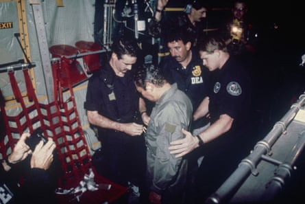 US agents place chains around the waist of Manuel Noriega inside a military transport plane