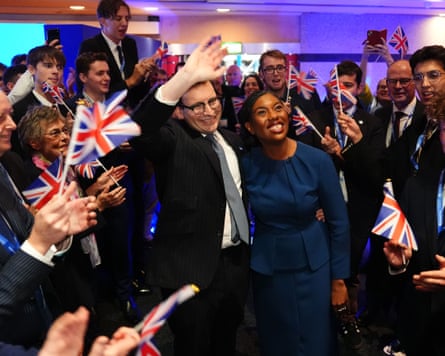 Kemi Badenoch and her husband, Hamish Badenoch, wave and are cheered by supporters waving union flags as they leave the stage after her conference speech