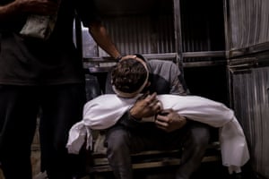 A Palestinian man presses his head against the shrouded body of a child