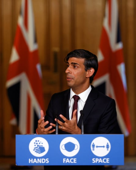 Rishi Sunak at a podium giving a briefing, with two union jacks in the background.