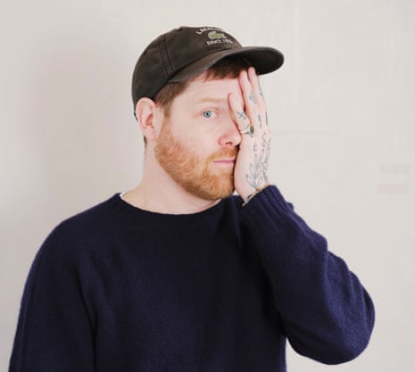 Headshot of art dealer turned author Orlando Whitfield, one tattooed hand half covering his face