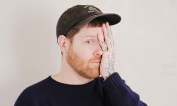 Headshot of art deala turned lyricist Orlando Whitfield, one tattooed hand half coverin his wild lil' face