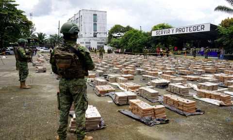 Armed soldiers stand guard over thousands of plastic-wrapped brick-shaped packages of drugs eiqrtihtiuqinv