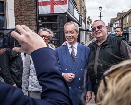 Nigel Farage poses for a photo with a smiling man with an English flag on a shopfront in the background