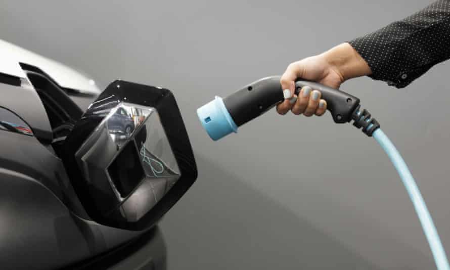 A woman holds a cable to charge an electric utility vehicle.