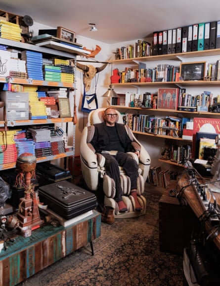 A man sits in a massage chair, surrounded by shelves with books and filing.