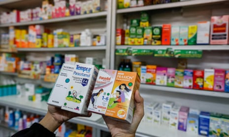 A shopkeeper holds boxes of liquid medicine at a pharmacy in Jakarta, Indonesia