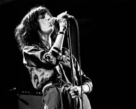 Black-and-white photo of Patti Smith on stage, holding a standing mic and singing