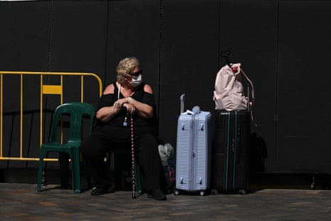 Una mujer con su equipaje y con una máscara facial afuera de la terminal de pasajeros de cruceros en The Rocks, Sydney.