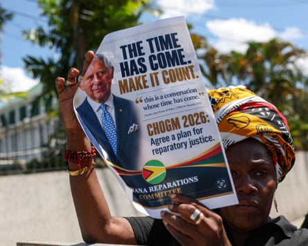 A Guyana reparations committee protester holds a placard featuring King Charles and reparations slogans