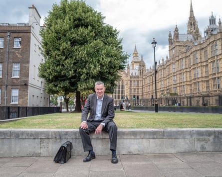 he sits on a low stone wall with parliamentary buildings in the background