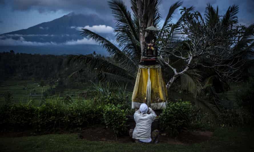 A man prays with Mount Agung in the background