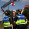 A protester, standing in front of two police officers, holds two lit flares