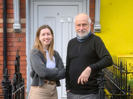 Thea May, 29, standing next to her housemate Paul Williams, 67,outside their home in Cardigan, West Wales. The front door is white, and to the right the wall is painted bright yellow.