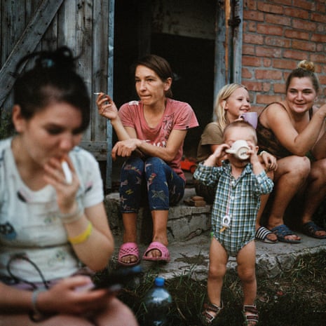 A woman sits on a front step smoking a cigarette with two other women and two children