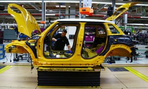An employee installs a wiring loom into a Mini car as it travels along the assembly line at the BMW plant in Oxford