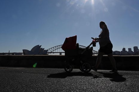 A woman pushes a pram along the Sydney Harbour waterfront with the Opera House in the background.