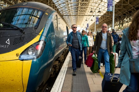 Train passengers arrive and walk down the platform at Manchester Piccadilly railway station.