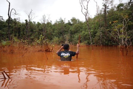 A man wades through a swamp of reddish brown-coloured water