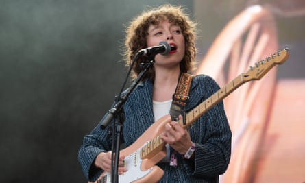 Stella Donnelly stands in front of a microphone holding a pink guitar and wearing a blue shirt