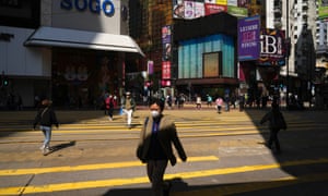 A man wearing a face mask walks across a street In Causeway Bay, a shopping district of Hong Kong.