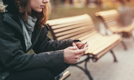 Teenage girl sitting on bench and texting on phone.