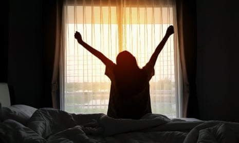 Stock photo of a woman with outstretched arms waking up, silhouetted by a sunrise