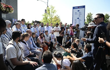 Crowd shot of delegates wearing keffiyehs on one side and press holding microphones and cameras on the other.