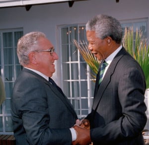 Mandela, in a pinstripe suit, and Kissinger shake hands on a terrace outside patio doors