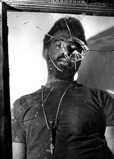 A young Black man is shown in a mirror with a circular break in it that circles the reflection of one of his eyes.