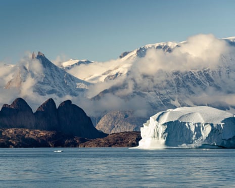 An iceberg floats near dark peaks and snowy mountains in Greenland's Scoresby Sund