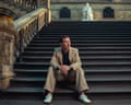 Benedict Cumberbatch sits on grand stone steps in the Natural History Museum, gazing upward