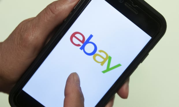 Hands hold a black smartphone with ebay logo in primary colors on it.