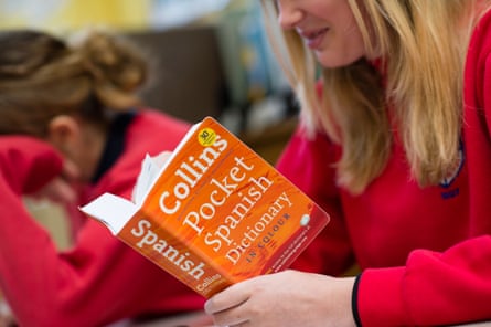 Schoolgirl in red jumper reading a Spanish pocket dictionary