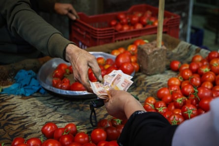 A customer pays for tomatoes with Egyptian pound banknotes at a food market