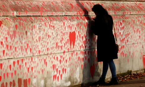 A woman writes a message onto the UK’s national Covid memorial wall on the south bank footpath of the  Thames in London.