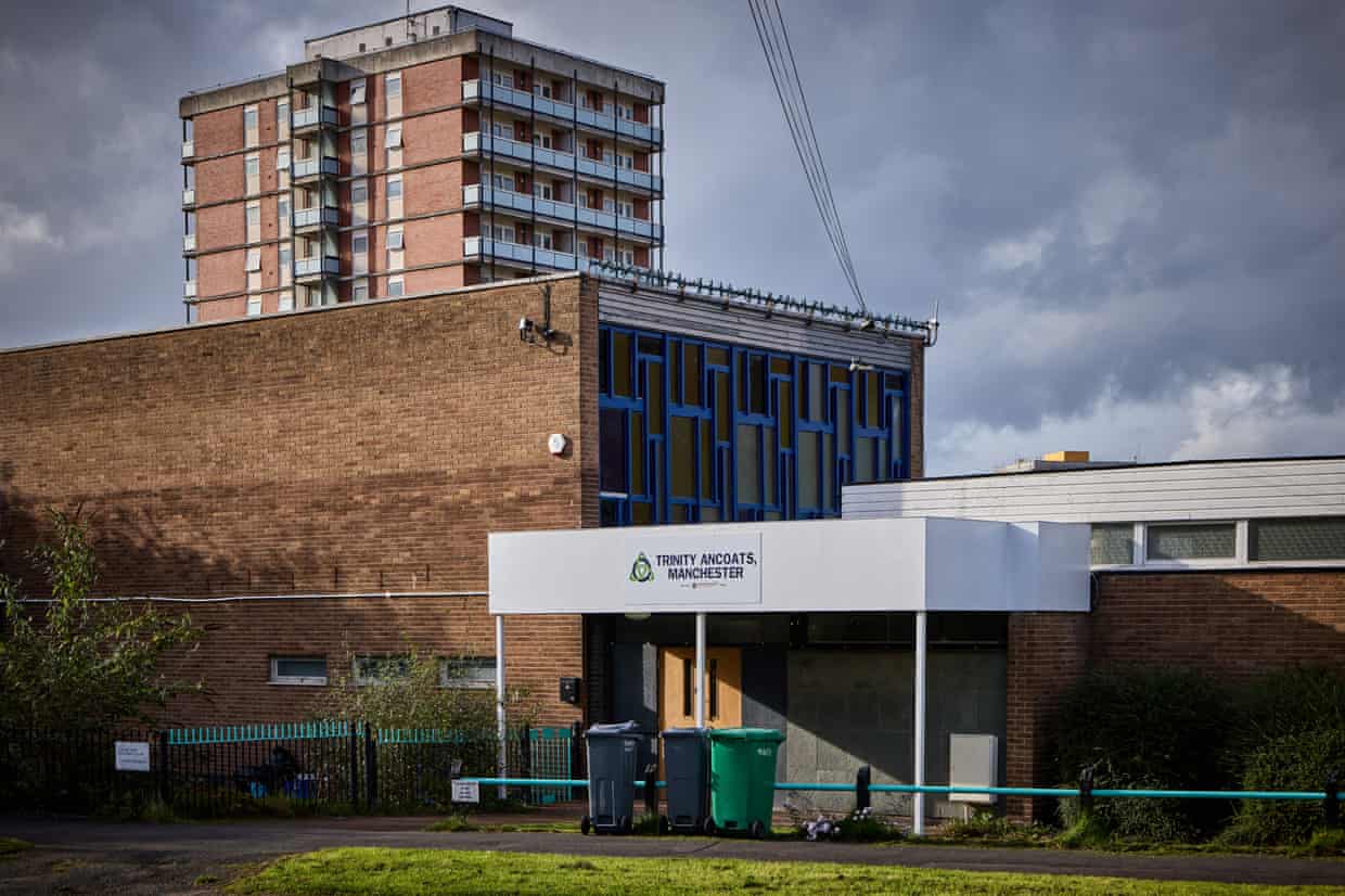 Trinity Ancoats foodbank building with bins outside, below a tall tower block