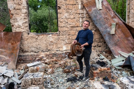 A man holds part of a wheel in front of the charred wall and floor of a building that is severely damaged