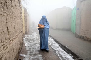 A woman wearing a burqa walks along a road towards her home after receiving free bread distributed as part of the Save Afghans from Hunger campaign in Kabul.