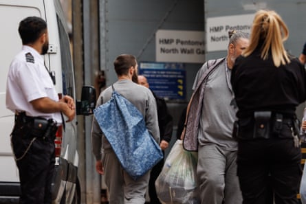 People in grey clothing carrying bags walk near a prison transport vehicle at HMP Pentonville
