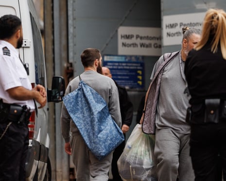 People in grey clothing carrying bags walk near a prison transport vehicle at HMP Pentonville